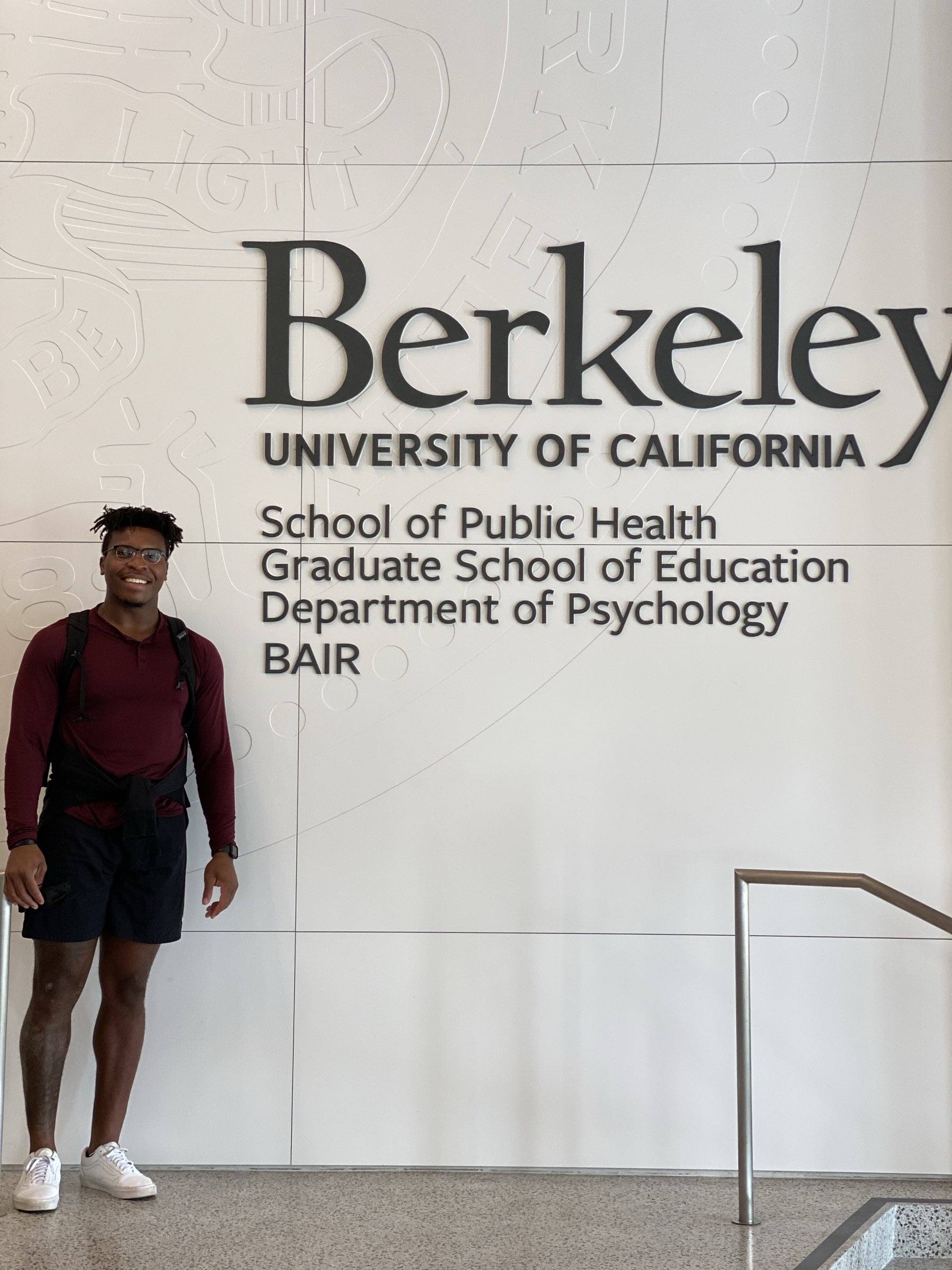 Marqez Bimage standing beside the UC Berkeley wall listing the School of Public Health, Graduate School of Education, Department of Psychology, and BAIR