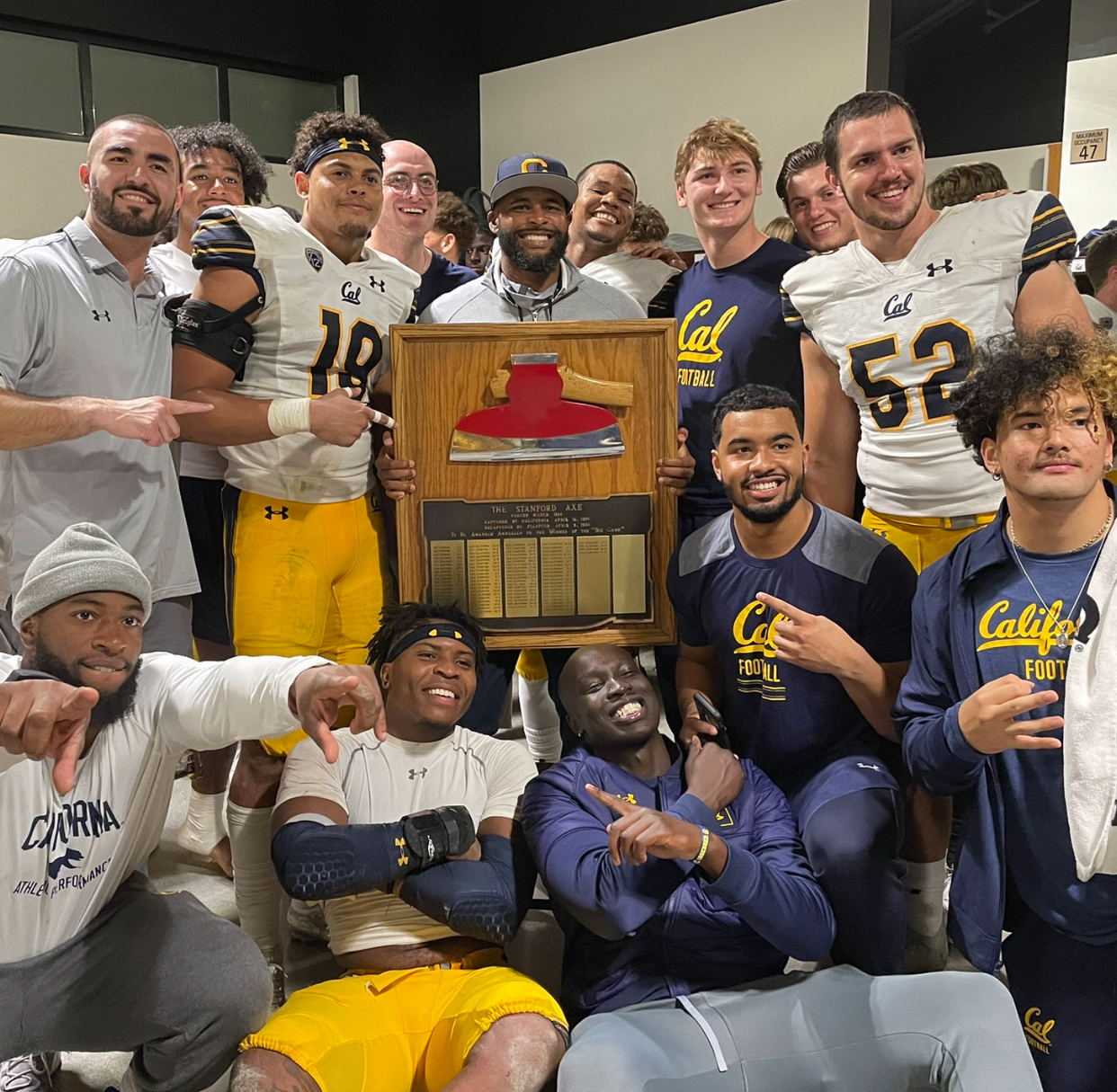 Marqez celebrating with the California Golden Bears team, holding the Stanford Axe trophy in the locker room